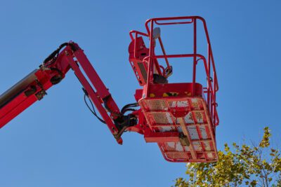 Hubarbeitsbühne mieten – so geht’s richtig Rote Arbeitsbühne vor blauem Himmel