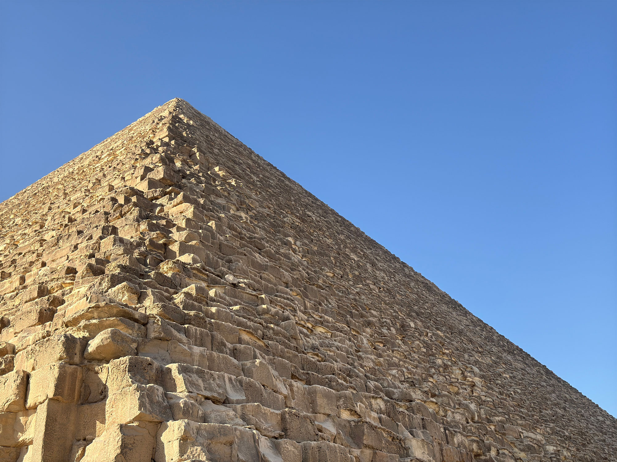 Nahaufnahme der Cheops-Pyramide in Gizeh mit freiliegenden Kalksteinbl&ouml;cken vor blauem Himmel.