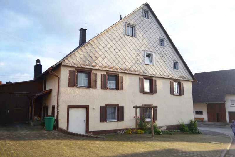 Älteres Wohnhaus mit steilem Satteldach, verschieferter Giebelfassade, mehreren Fenstern und sichtbaren Alterungsspuren an Dach und Außenwänden.