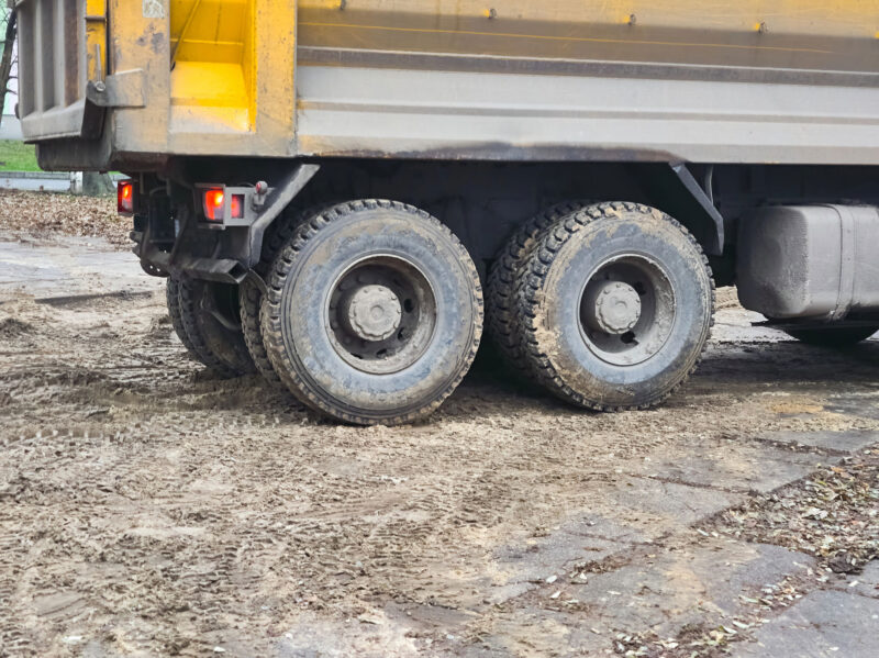 Hinterräder eines schweren Baustellen-Lkw auf weichem, von Reifenspuren gezeichnetem Untergrund